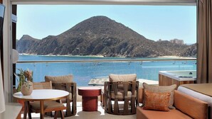 A balcony with a view of a mountain and sea, furnished with a sofa, chairs, and a small table.