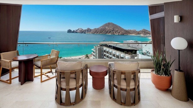 A balcony with wicker furniture, a potted plant, and a view of the sea and mountains.