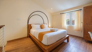 A bedroom with a wooden bed, a bench, a wardrobe, and a window with curtains. - Cove Lotus Loft Seminyak (Keroboken Kelod)