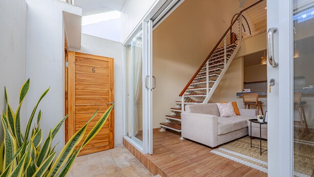 A modern interior with a wooden door, a staircase, a white sofa, and a potted plant. - Cove Lotus Loft Seminyak (Keroboken Kelod)