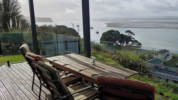 Eine Holzterrasse mit Sitzgelegenheiten im Freien, mit Blick auf eine Küstenlandschaft mit Häusern und Meer.