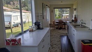 Eine kompakte Küche mit Essbereich, großen Fenstern und Blick auf Reisemobile vor dem Haus.