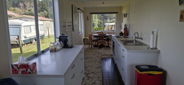 A compact kitchen with a dining area, large windows, and a view of parked caravans outside. - Glorious views and relaxation a plenty (Kawhia)