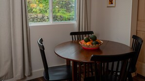 A dining table with a fruit basket, four chairs, a window with curtains, and a framed picture on the wall. - Beautiful Apartment in Hawaii (Captain Cook)