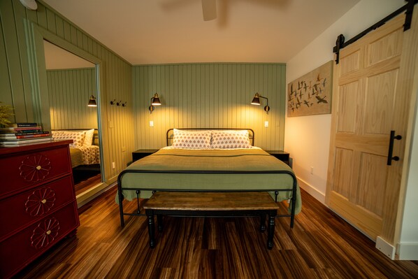 A bedroom with a bed, bedside tables, a dresser, a bench, a mirror, and a door.