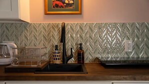 A kitchen with a modern sink, a coffee machine, and a decorative wall with a chevron pattern. - Beautiful Apartment in Hawaii (Captain Cook)