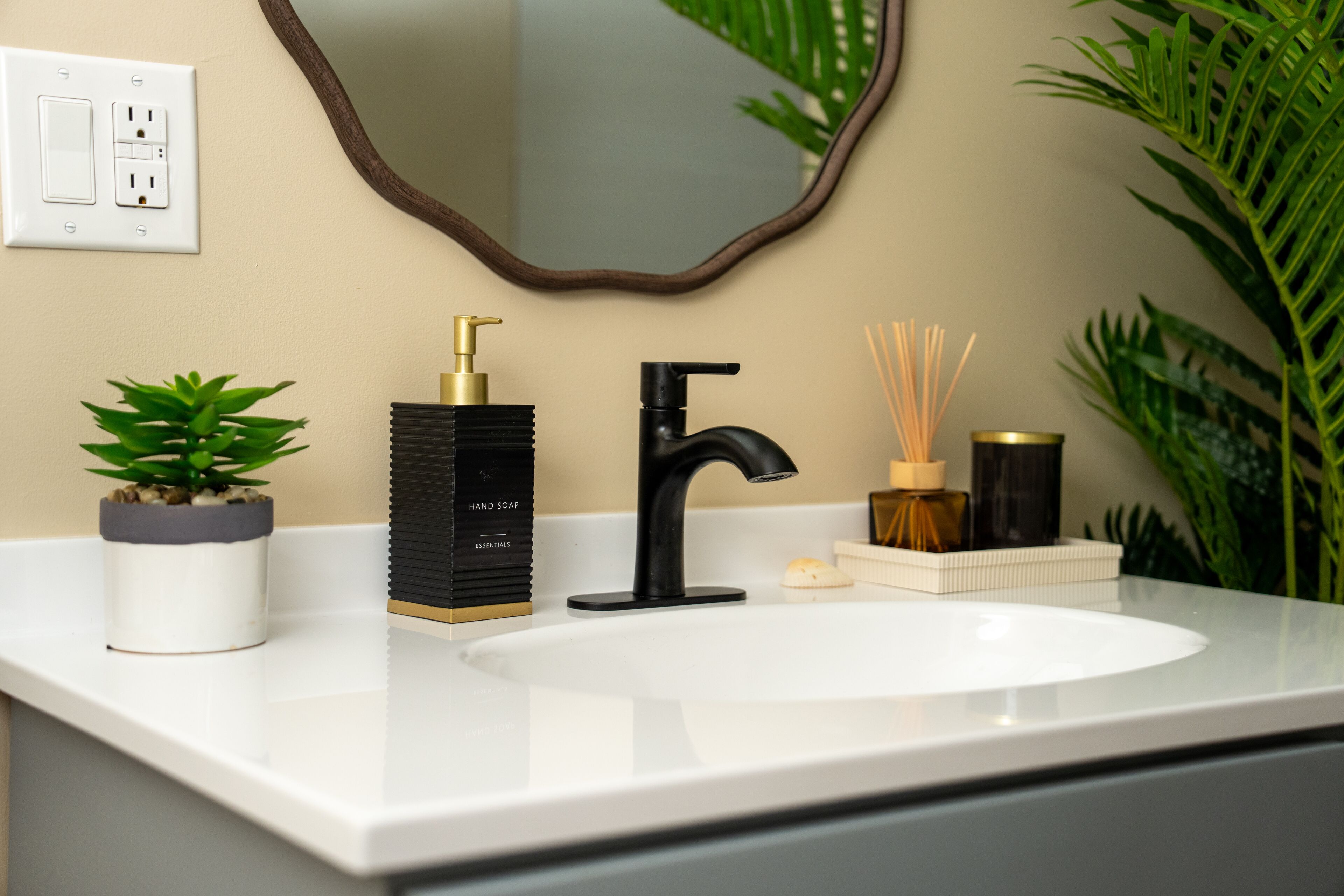 A bathroom with a white sink, a black faucet, a gold soap dispenser, and a mirror with a wooden frame.