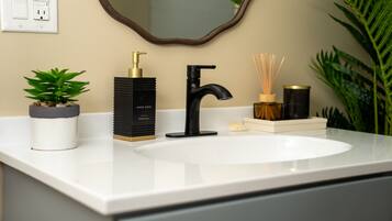 A bathroom with a white sink, a black faucet, a gold soap dispenser, and a mirror with a wooden frame.