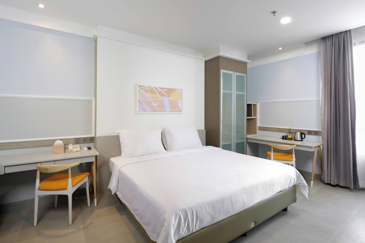 A hotel room with a bed, a desk, a chair, a wardrobe, and a bathroom.