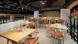 A modern restaurant with multiple wooden tables and chairs, a high ceiling with exposed pipes, and a view through a glass partition. - Joylive BSD City (Pagedangan)