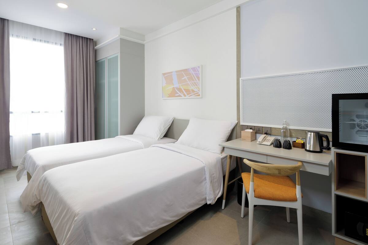 A hotel room with two beds, a desk with a telephone, a kettle, and a television.