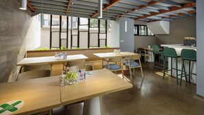 A modern restaurant with wooden tables and chairs, a bar area, and large windows allowing natural light. - Joylive BSD City (Pagedangan)