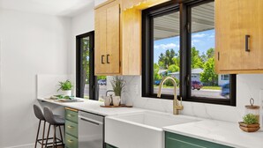 A modern kitchen with a white countertop, green cabinets, and a large window with a view of the street.