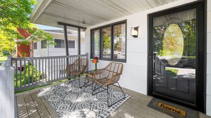 A covered porch with two wicker chairs, a patterned rug, and a 'home' doormat.