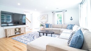 A modern living room with a flat-screen TV, a beige sofa, a coffee table, and a patterned rug.