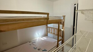 Une petite pièce unique, avec des lits superposés, un plafond blanc et un aménagement simple et fonctionnel.
