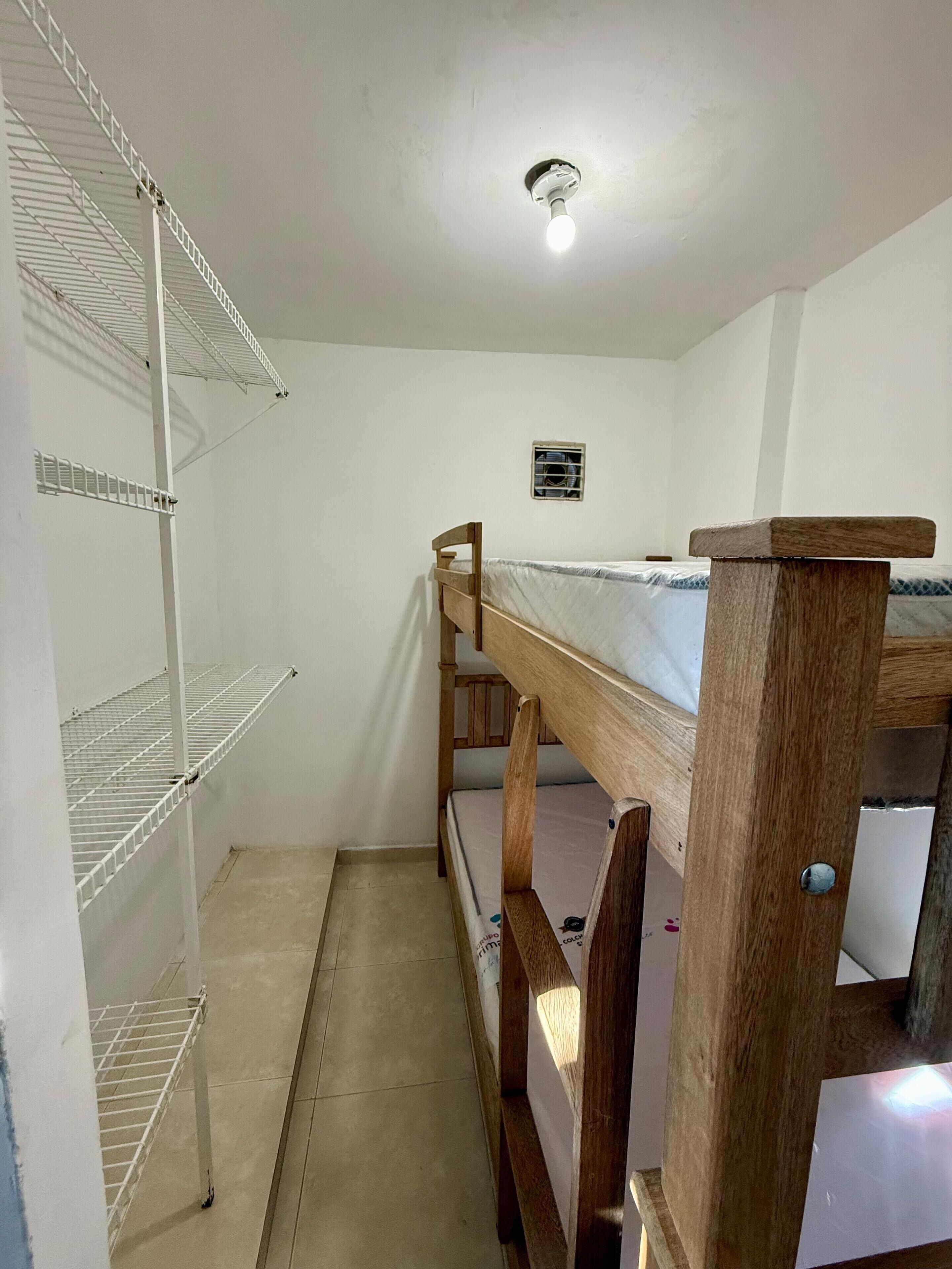 A bunk bed room with white walls, a ceiling light, and a small air conditioning unit.