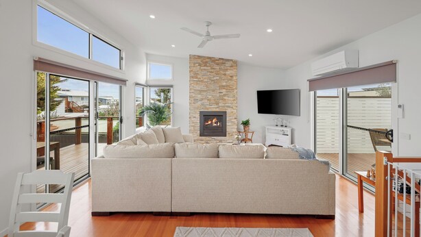Un salon moderne avec un canapé d’angle, une cheminée, un ventilateur de plafond et de grandes fenêtres.