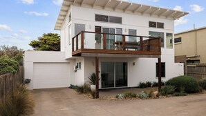 Une maison moderne à deux étages, dotée d’un balcon, de grandes fenêtres et d’un garage.