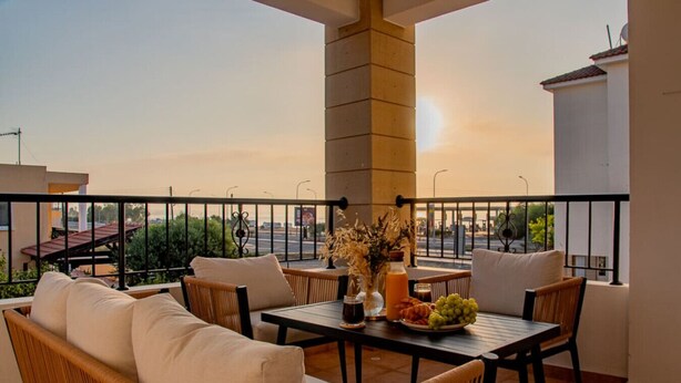 A balcony with wicker furniture, a table with a fruit bowl, and a vase with flowers. - TelMar Sunrise View - 100m from the Sea (Livadia)