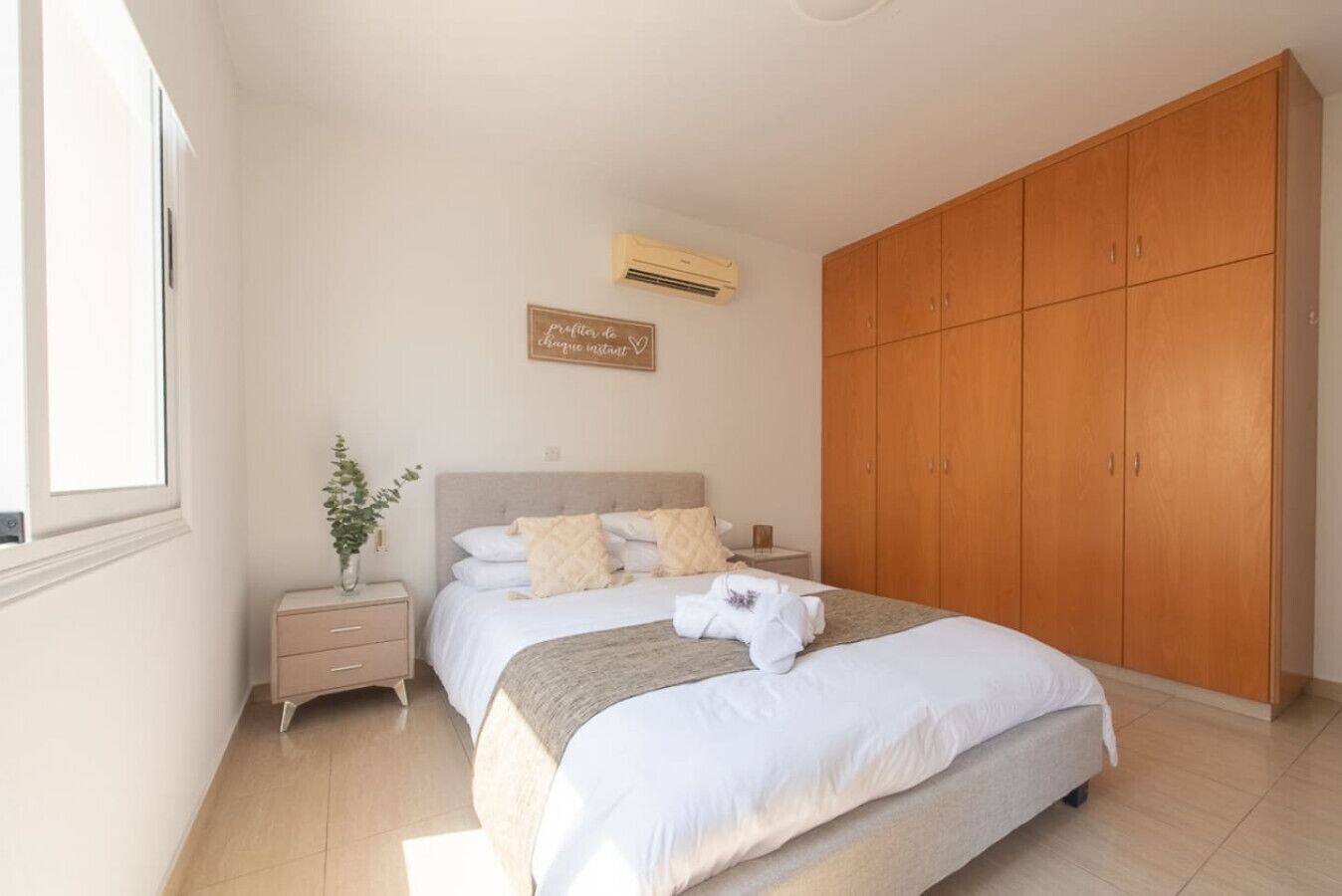 Ein Schlafzimmer mit Bett, Nachttisch, Kleiderschrank und Wandairconditioner.