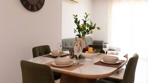 A dining area with a round table set for four, surrounded by green upholstered chairs. A bowl of fruit and a bottle of wine are on the table. - TelMar Sunrise View - 100m from the Sea (Livadia)