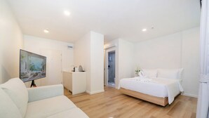 A modern hotel room with a bed, a sofa, a TV, and a bathroom visible through an open door. - Zcape X2 Condominium in Bang Tao (Choeng Thale)