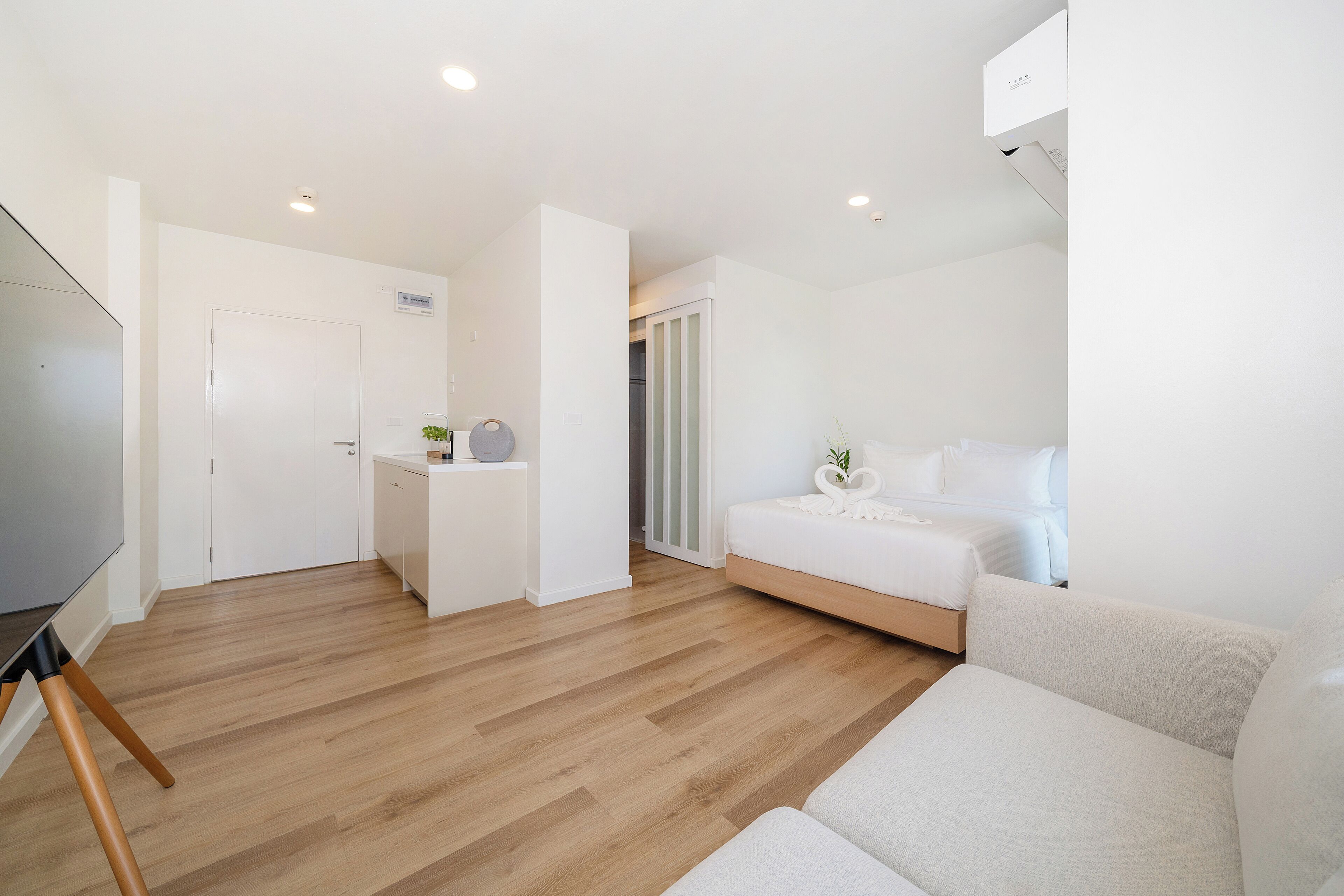 A modern, minimalist bedroom with a bed, a small desk, and a TV.