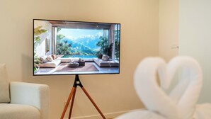 A modern living room with a large flat-screen TV on a tripod, a sofa, and a chair. - Zcape X2 Condominium in Bang Tao (Choeng Thale)