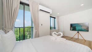 A hotel room with a large bed, a balcony with curtains, a mounted TV, and a painting on the wall. - Zcape X2 Condominium in Bang Tao (Choeng Thale)