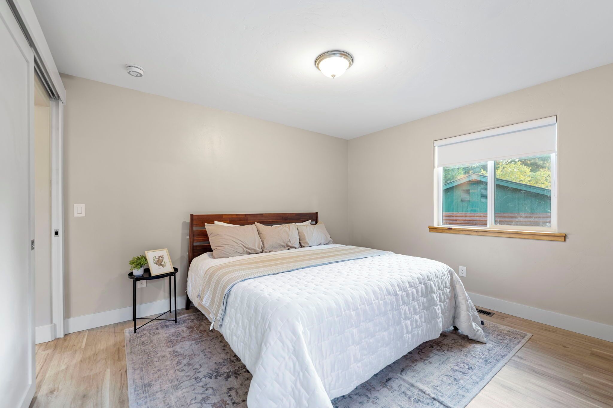 A bedroom with a bed, a nightstand, a window, and a door.