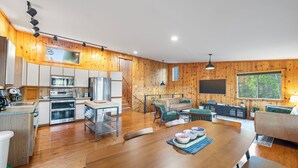 Un'ampia cucina con pareti in legno, una zona pranzo con un tavolo grande e un accogliente soggiorno con divano e TV.