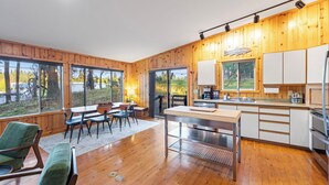 Una cucina moderna con pareti in legno, un'area pranzo con sedie e un tavolo, e ampie finestre che offrono vista sull'esterno.