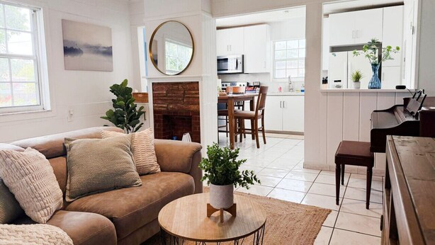 A living room with a brown sofa, a round coffee table, and a fireplace. There is a dining area with a table and chairs in the background.