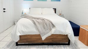 A bedroom with a bed, bedside tables, a bench, and artwork on the wall.