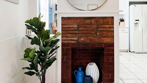 A modern kitchen with a white tiled floor, a brick fireplace, and a large mirror above it.