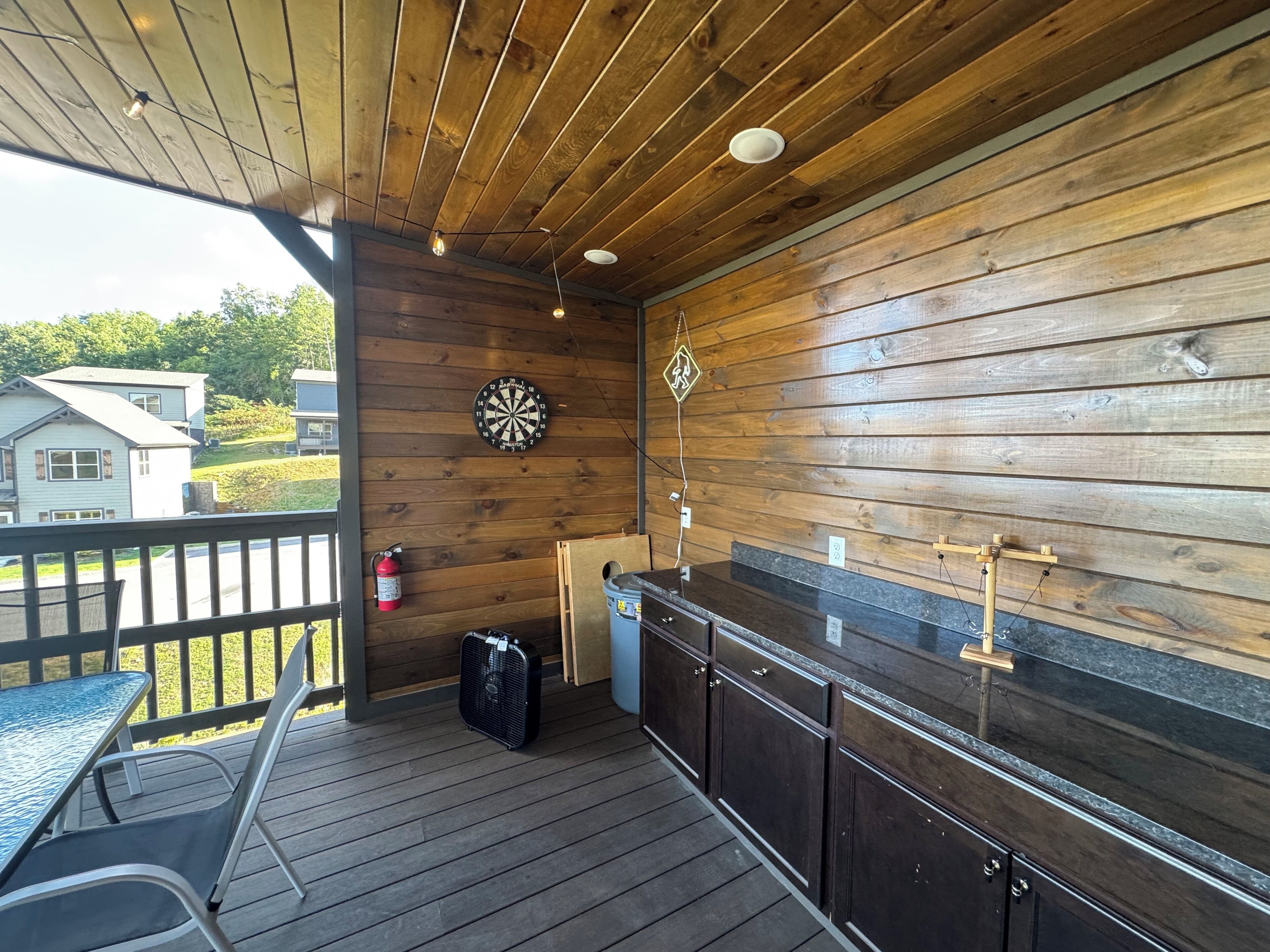 Un espacio al aire libre cubierto con una terraza de madera, un dardo, un extintor, un ventilador y una barra.