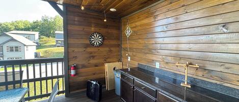 Un espacio al aire libre cubierto con una terraza de madera, un dardo, un extintor, un ventilador y una barra.