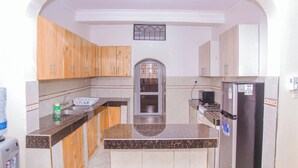 A kitchen with wooden cabinets, a marble countertop, a refrigerator, and a microwave. - Lovely Villa in Kilifi with Stunning Views (Kilifi)