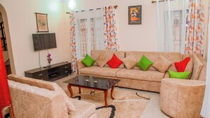 A living room with a beige sofa, a glass coffee table, and a dark entertainment unit. - Lovely Villa in Kilifi with Stunning Views (Kilifi)