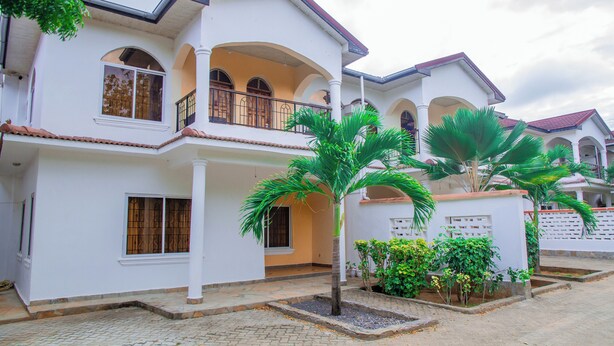 A two-story house with a balcony, a tiled roof, and a garden with palm trees. - Lovely Villa in Kilifi with Stunning Views (Kilifi)