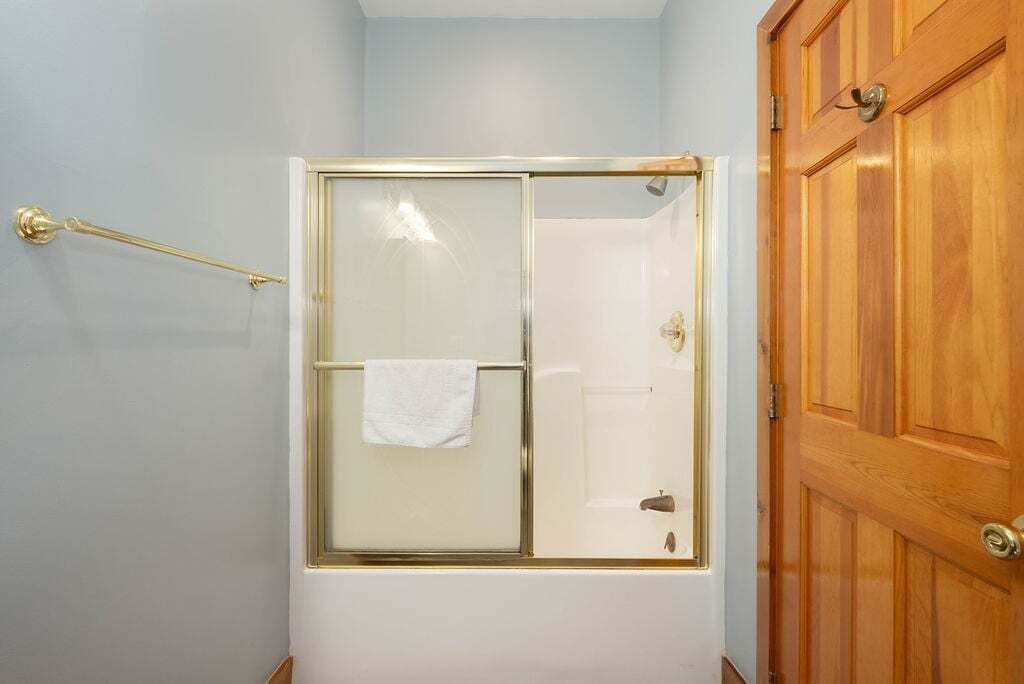 Een douche met een glazen deur, een handdoek hangend aan de deur en een houten deur rechts.