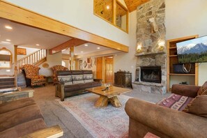 A spacious living area with a stone fireplace, a television, and a staircase leading to an upper level.