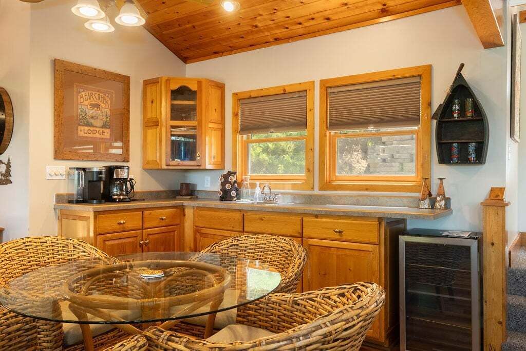 A kitchen with wooden cabinets, a glass-top table, wicker chairs, and a refrigerator.