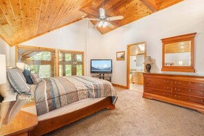 Um quarto com cama, televisão, penteadeira e ventilador de teto.