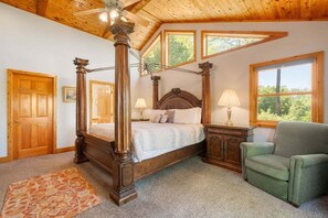 A four-poster bed with a wooden headboard, a green armchair, and a small cabinet with a lamp.