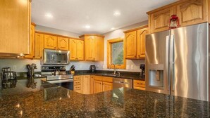 Una cocina con encimeras de granito, armarios de madera y electrodomésticos de acero inoxidable, además de un ventanal.