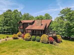 A wooden cabin with a porch, surrounded by a well-maintained lawn and colorful shrubs.