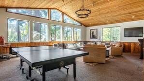Une pièce spacieuse équipée d’une table de ping-pong, de nombreuses fenêtres et d’un grand téléviseur.