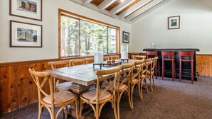 Un coin repas avec une table et des chaises en bois, des tableaux encadrés aux murs et une vue sur les arbres à travers de grandes fenêtres.